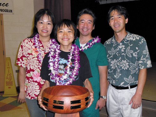 Akira Takabayashi, flanked by his parents, Yoko and Eric, proudly shows off his Hawaii Spelling Bee trophy. With them is Dave Hinazumi (right) of Grove Farm | Photos from Dara Young