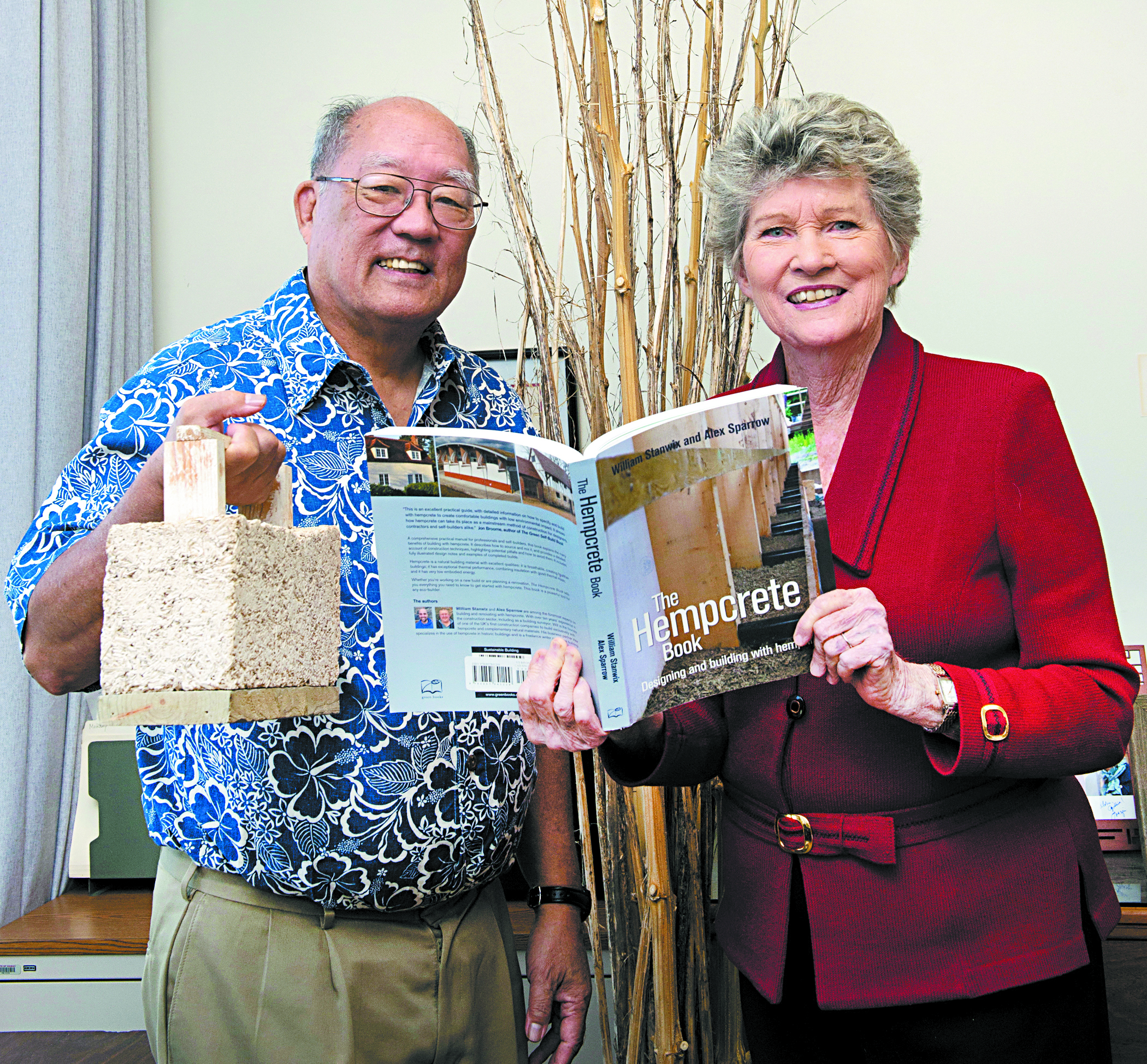 Industrial hemp research project principal investigator Harry Ako, Ph.D., and longtime industrial hemp proponent state Rep. Cynthia Thielen with a hempcrete sample and a book. Behind them are hemp stalks  
